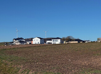 Houses with solar panels on roof and wind turbines nearby. Summer landscape with green vineyard....