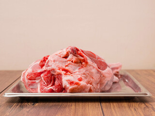 Fresh raw leg of lamb is on a silver stainless tray which is on a wooden table. Premium high...