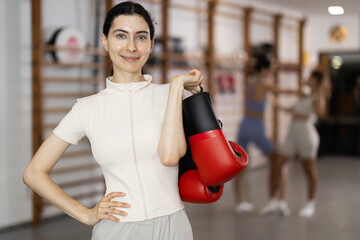 Young woman in sportswear and boxing gloves stands in the gym against the background of people...