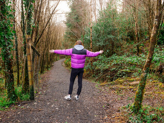 Female jogger standing on a foot path in a dense forest park. Woman with her hands up in the air....