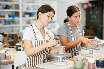 During working day, two pottery workshop visitors sculpt from raw clay. They smooth surface of...