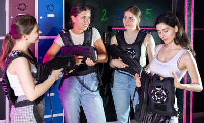 Group of girls in laser tag vests with rifles in their hands are discussing the rules of the game...