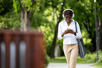 Beautiful black woman walking through the park and using smart phone.