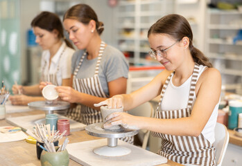 Adolescence girl student sits near desktop and doing from clay product. Lover of applied art...