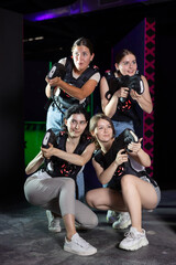 Smiling young girlfriends playing laser tag game with colored laser