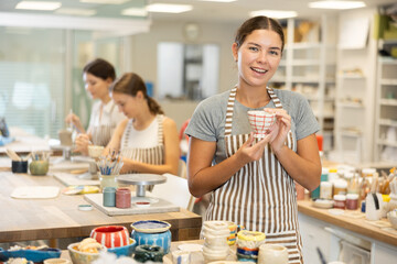 In pottery workshop, girl holds finished vase made of clay, demonstrates successfully completed...