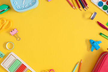 Back to school. Art frame made of colorful school stationery, including an alarm clock, play dough, pencils and paints on a yellow background. Perfect for educational themes.
