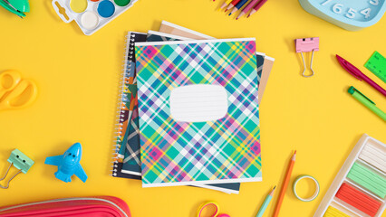 Back to school background. School bright supplies in the center of the composition a stack of notebooks, as well as pencils, paints and much more placed on a yellow background.