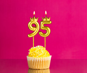 Birthday celebration with number 95 candle - Yellow cupcake on a pink background