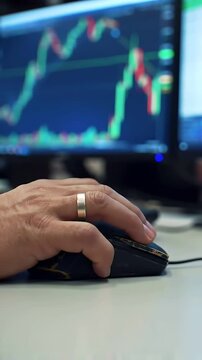 Intense Trading Action: A traders hand grips the mouse, clicking rapidly as stock market charts with fluctuating red and green candlestick patterns surge on the screen.