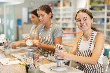 Young woman teacher and two girls students sculpt from clay and paint pottery