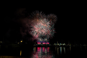 Colorful fireworks exploding over a marina at night, reflected in the calm harbor water with yachts...