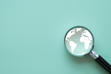 Global research concept. A magnifying glass focusing on a world map symbol on a green background....