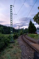 Railway line curving through countryside with electric poles and forest background. Rural train infrastructure at dusk.
