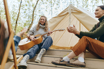 Middle age woman playing guitar outdoors with friends enjoying active, healthy lifestyle and...