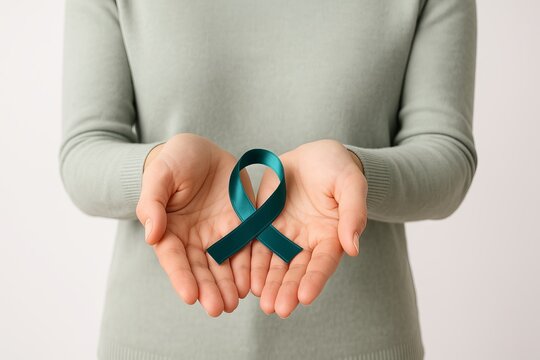 Woman holding teal awareness ribbon in cupped hands against white background. Concept of ovarian cancer support, sexual assault awareness, PCOS and PTSD prevention, anxiety disorders