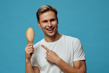 Happy smiling young man with short brown hair wearing plain white t-shirt holding a hairbrush...