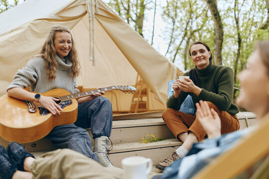 Middle age woman playing guitar with friends outdoors, active and healthy lifestyle enjoying community and wellness in nature, promoting wellbeing and fitness.