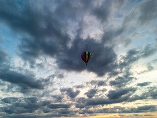 Colorful hot air balloon flying through dramatic cloudy sky at sunset