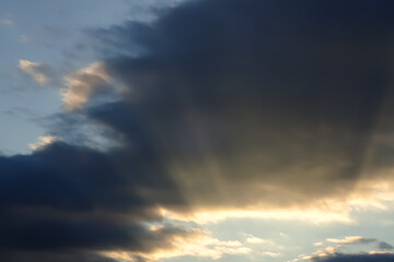 Dramatic sunset clouds with light rays shining through the atmosphere. Abstract sky background with soft contrast and natural light in motion