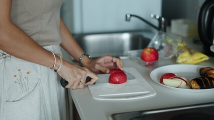 Female preparing fresh red apple slice on wooden cutting board, kitchen countertop morning meal...