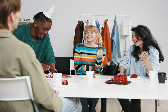 Young adult woman and colleagues socializing at workplace with cake, celebrating in a casual business environment, representing Gen Z coworkers and friends.