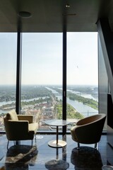 This stylish lounge features two elegant chairs by a large window, offering breathtaking views of a vibrant cityscape and picturesque waterways, blending comfort with stunning aesthetics