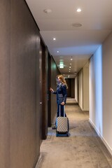 A fashionable woman stands beside her suitcase, ready to enter her stylish hotel room in a sleek...