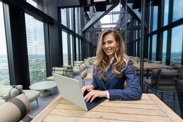 A confident and ambitious businesswoman is focused on her laptop in a stylish, modern office with...