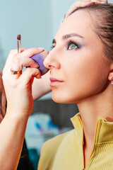 Obraz premium Makeup artist applying make up to a beautiful young pretty girl in a professional salon. Beauty, fashion and skin care industry. The work of a makeup artist. Applying a base or foundation to the face.