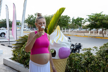 Pregnant woman enjoying an ice cream cone on the street. Standing next to large ice cream cone...