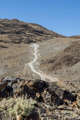 Winding dirt road traverses arid landscape, surrounded by rocky terrain and sparse vegetation,...