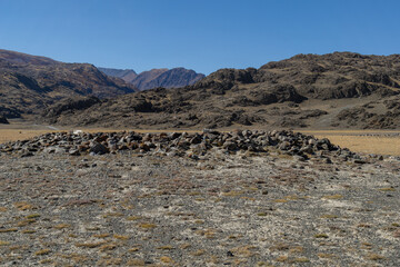 Rocky landscape with a stone formation in the foreground, surrounded by rugged mountains and clear...