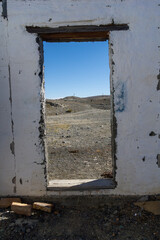 Abandoned building doorway frames a vast, arid landscape under a clear blue sky, showcasing the contrast between man-made structures and natural surroundings