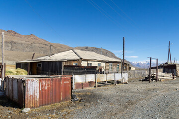 Rustic wooden house surrounded by fences and outbuildings in a remote mountainous area, showcasing...