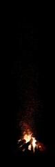 Campfire burning at night with glowing sparks rising into the dark sky. Atmospheric image perfect...