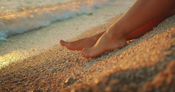 Woman sits on beach with feet in pebbles during sunset in summer Croatia