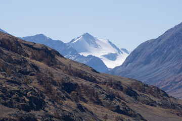 Majestic snow-capped mountain peaks rise above rugged terrain, surrounded by rocky slopes and clear...