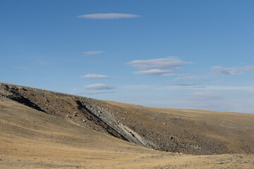 Expansive dry landscape featuring rolling hills under a clear blue sky with scattered clouds,...