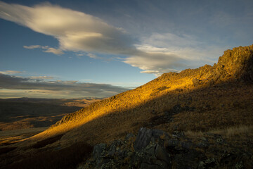 Scenic landscape featuring rolling hills bathed in golden sunlight, with dramatic clouds overhead, showcasing the beauty of nature and the tranquility of the outdoors