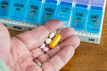 Closeup of man holding pills with pills case in the background