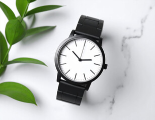 Minimalist wristwatch with black strap and white face placed on marble surface alongside green leaves, creating serene and stylish atmosphere