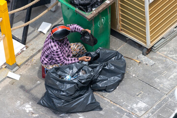 An old woman searches through a garbage bin and collect recycle items, Vietnam