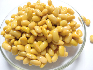 Fresh yellow soybeans in a clear glass bowl on a plain white background. Shiny and neatly arranged beans, perfect for food ingredients, healthy eating, and vegetarian lifestyle concepts.