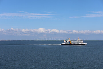 Ferry cruising across calm waters with wind turbines in the background on a clear day