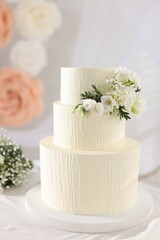 Delicious wedding cake with floral decor and bouquet on table indoors
