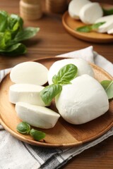 Pieces of delicious mozzarella cheese and basil leaves on wooden table, closeup
