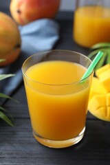 Tasty mango juice in glass, fresh fruits and green leaves on wooden table, closeup