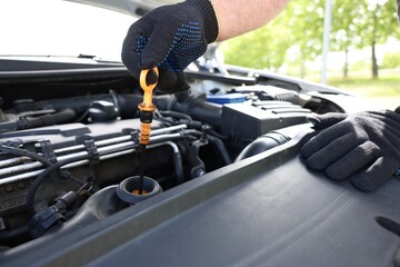 Worker checking motor oil level in car with dipstick, closeup