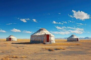 Three traditional round yurts standing on a vast dry grassland under a clear blue sky with scattered clouds, evoking a sense of tranquility and openness